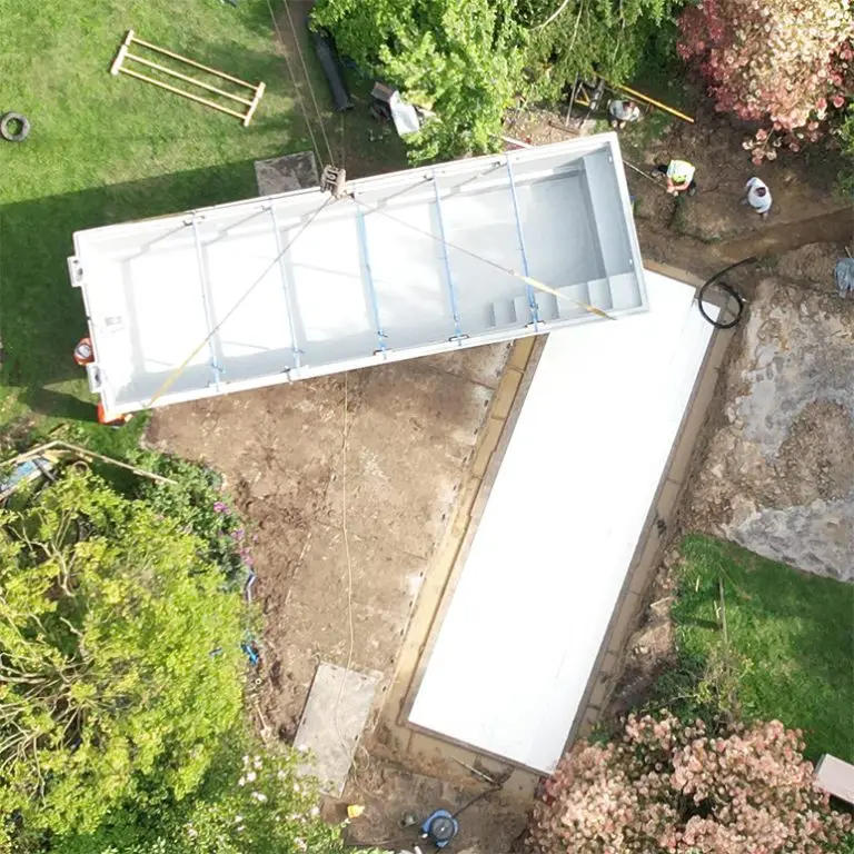 A one-piece swimming pool being lifted by a crane into position in a residential garden.