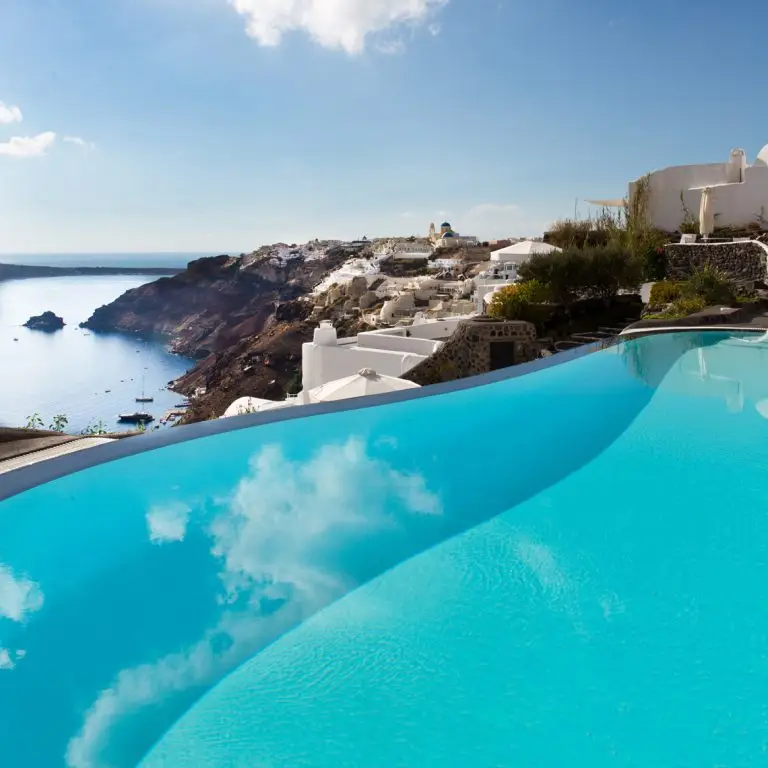 A luxurious infinity pool overlooking the Aegean Sea in Santorini, Greece, with white-washed architecture and clear blue skies.